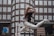 A person wearing a white outfit leaps gracefully in mid-air against a backdrop of an urban building with numerous windows. The motion captures a sense of freedom and dynamism, with the person's hair flowing and limbs extended in an elegant pose.