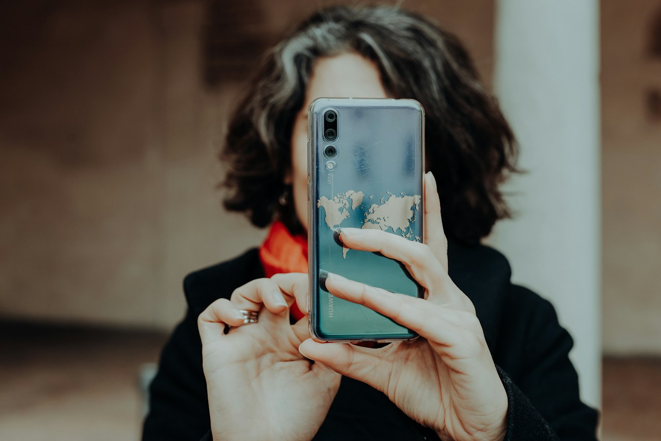 A person holds a smartphone (world-map case, rear camera facing out) directly in front of their face so the device completely covers and replaces