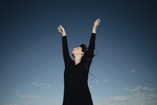 a woman in a black dress reaching up into the air