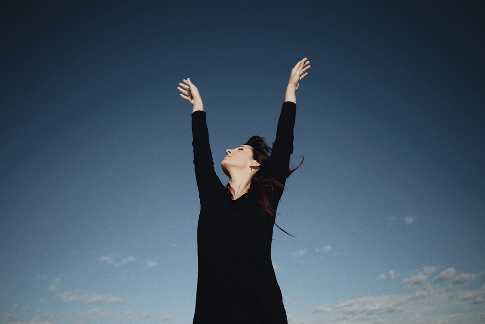 a woman in a black dress reaching up into the air