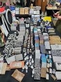 An assortment of sparkling and glittery accessories is displayed on a black table. The items include wallets, vanity cases, compact mirrors, and wristwatches, among others. Many pieces are embellished with rhinestones, sequins, and dazzling patterns. A variety of colors such as silver, gold, and multicolored designs are present, and the overall display is organized in a visually appealing manner. Some text made from shiny material is seen on the left side.