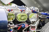 Close-up view of a car engine compartment showing multiple shiny chrome air filters labeled with a logo, connected with red and blue hoses and various metallic components. The focus is on the intricate and reflective engine parts under bright lighting.