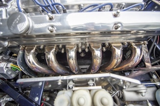 A close-up of a polished steel car engine with visible wires and components. The metallic surfaces are shiny and reflective, and the picture captures the intricate detailing and mechanical parts.