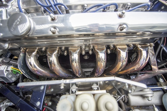 A close-up of a polished steel car engine with visible wires and components. The metallic surfaces are shiny and reflective, and the picture captures the intricate detailing and mechanical parts.