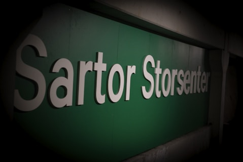Large white letters spell out 'Sartor Storsenter' on a green background, possibly indicating a shopping center or commercial establishment. The lighting is subdued, creating a sense of depth.
