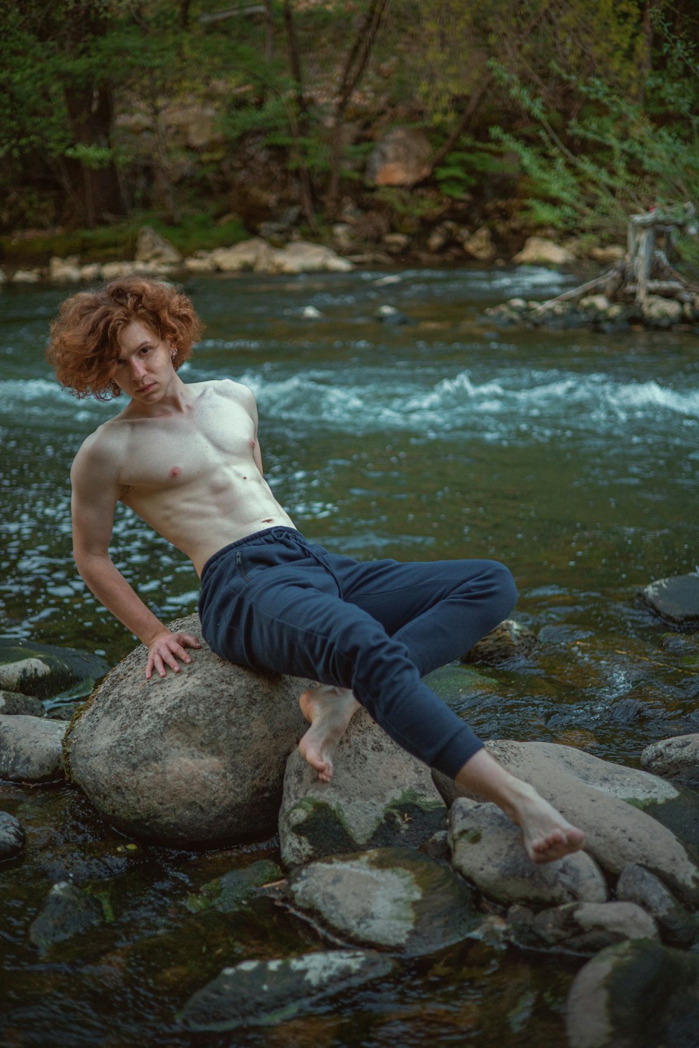 a shirtless man sitting on a rock in a river