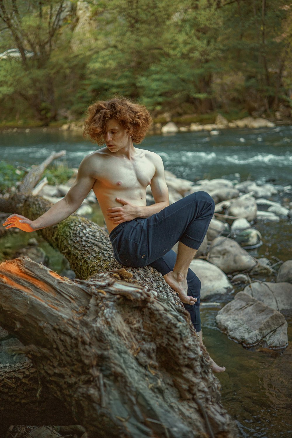 a shirtless man sitting on a log by a river