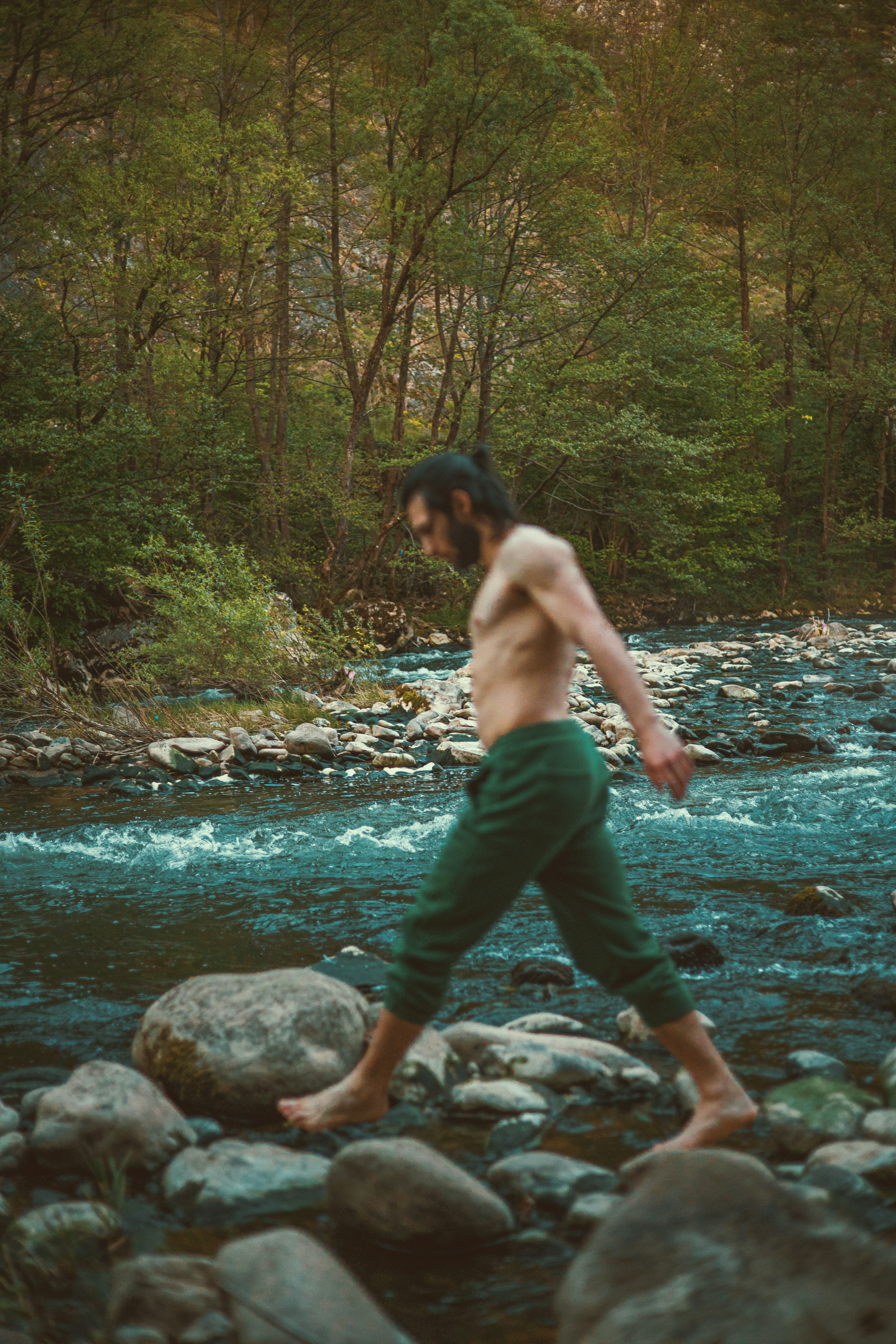 Man walking across rocky stream in forest