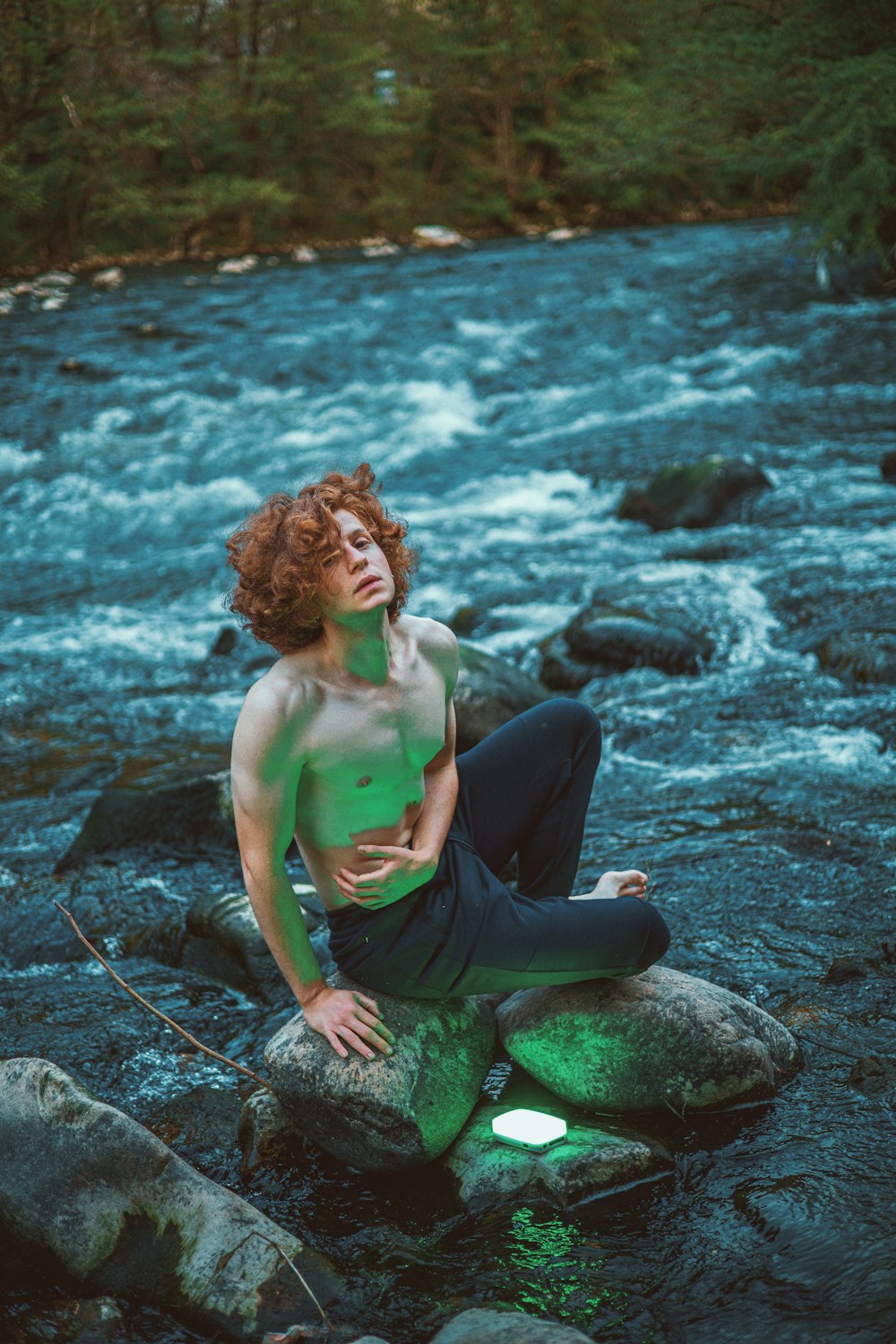 a man sitting on a rock next to a river