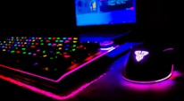 Close-up of a gamer’s hands on a glowing RGB keyboard with a pixelated game on screen.