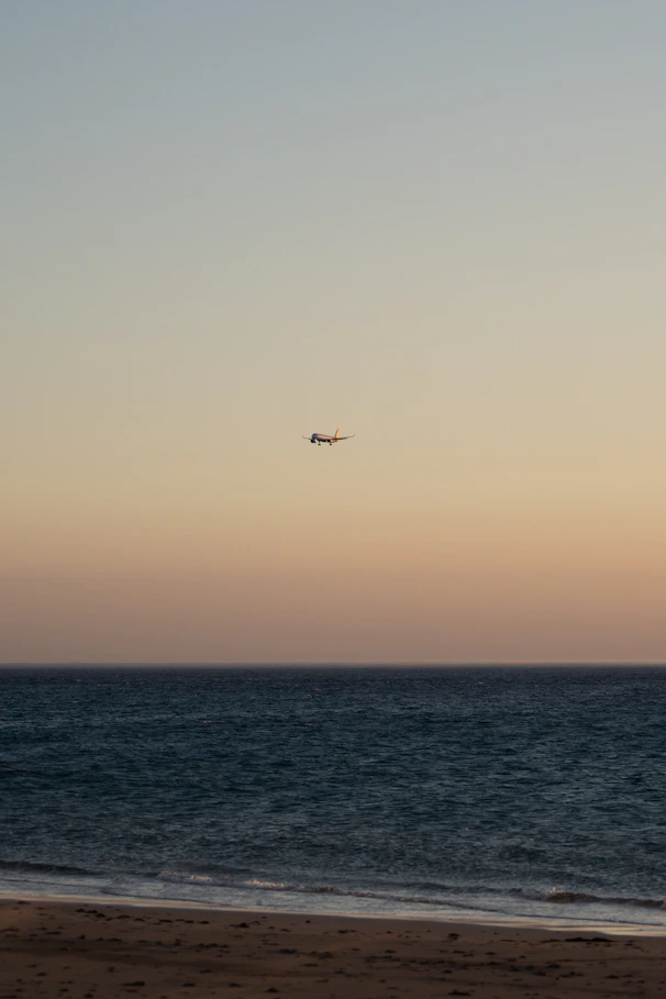 A warm-toned photo of a small plane flying over a rugged coastline at sunset.