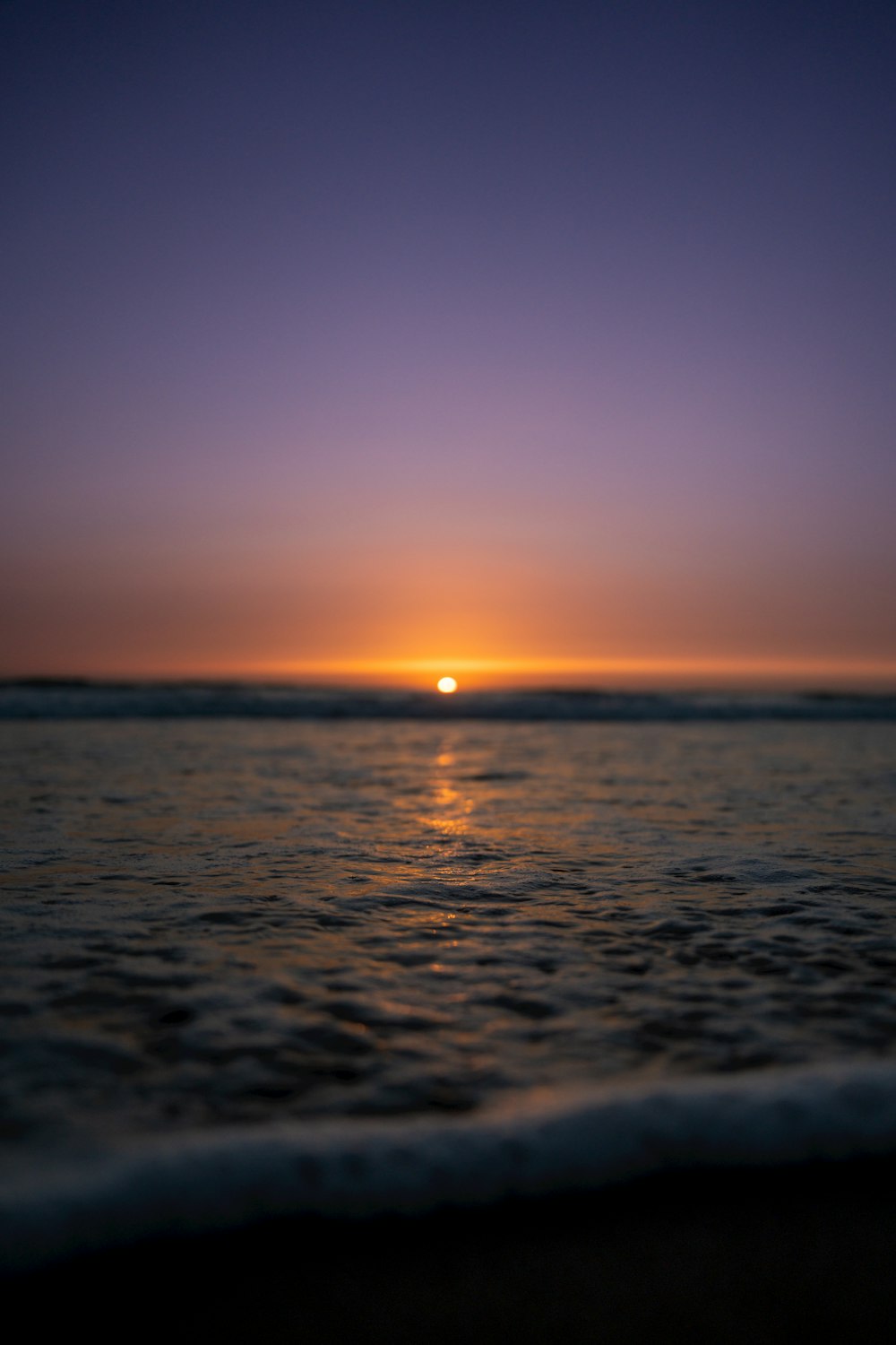 the sun is setting over the water at the beach