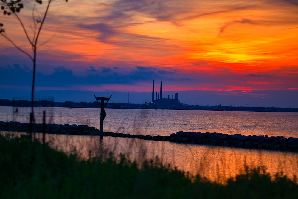 a sunset over a body of water with a power plant in the distance