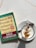 A copy of 'How to Win Friends & Influence People' by Dale Carnegie lies on a light-colored marble surface next to a cappuccino. The book cover is green and yellow with red accents, showing that it is a revised edition with over 15 million copies sold. The cappuccino is presented in a white cup on a saucer, featuring intricate latte art on top.