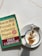 A copy of 'How to Win Friends & Influence People' by Dale Carnegie lies on a light-colored marble surface next to a cappuccino. The book cover is green and yellow with red accents, showing that it is a revised edition with over 15 million copies sold. The cappuccino is presented in a white cup on a saucer, featuring intricate latte art on top.