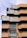 A modern architectural building with a layered and geometric design featuring brick and concrete materials. The façade includes terrace spaces with greenery and plants, offering a blend of natural elements with urban architecture. Large windows add to the contemporary aesthetic.