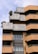 A modern architectural building with a layered and geometric design featuring brick and concrete materials. The façade includes terrace spaces with greenery and plants, offering a blend of natural elements with urban architecture. Large windows add to the contemporary aesthetic.