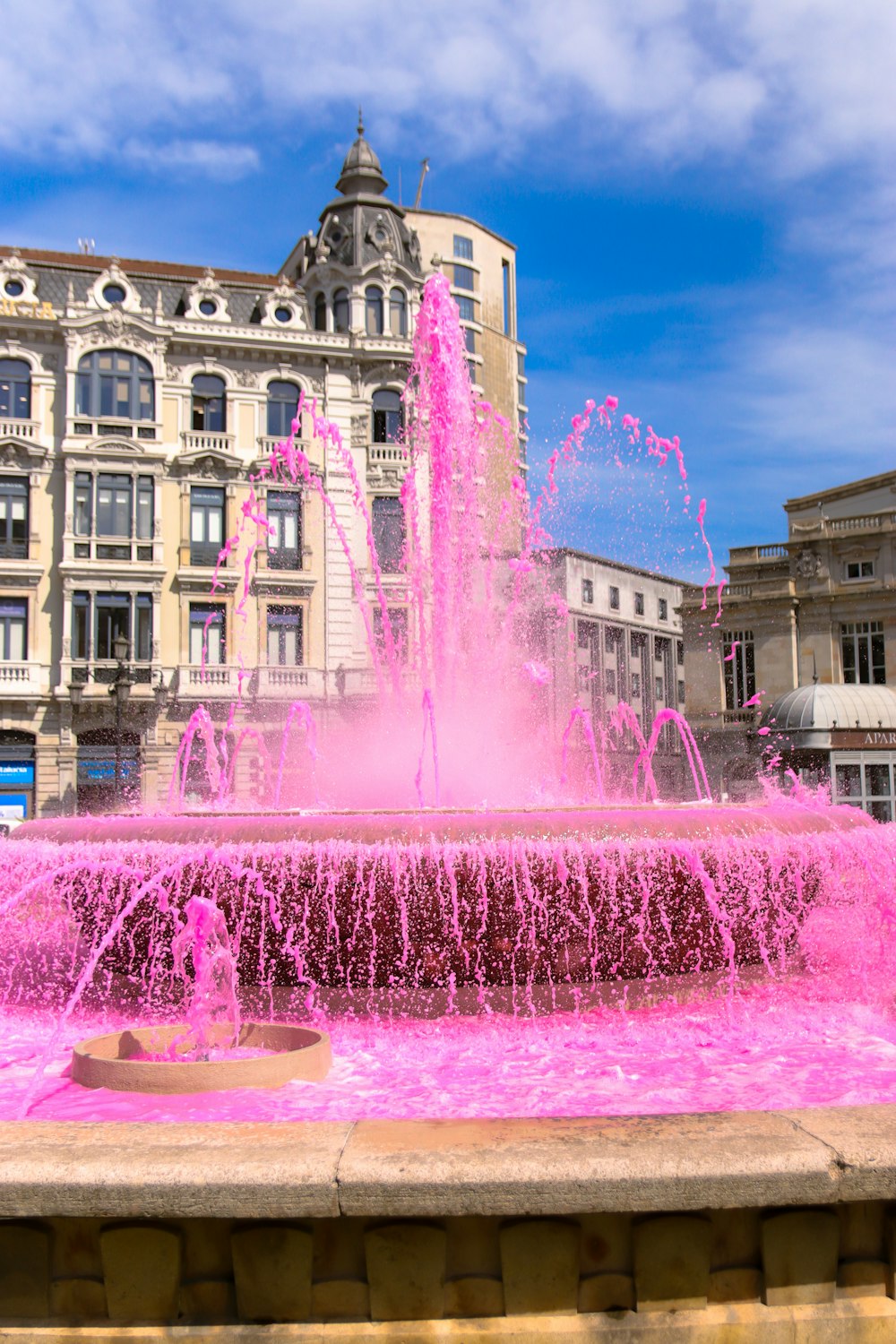 a pink fountain in front of a large building