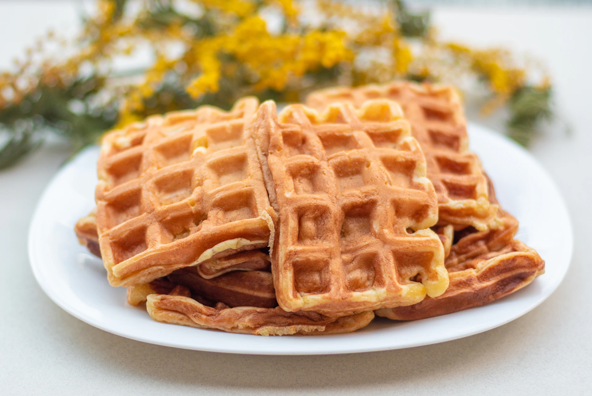 A stack of golden waffles topped with melting ice cream and fresh fruit, captured in warm natural light.