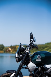 A vintage motorcycle parked beside a calm lake reflecting autumn trees.