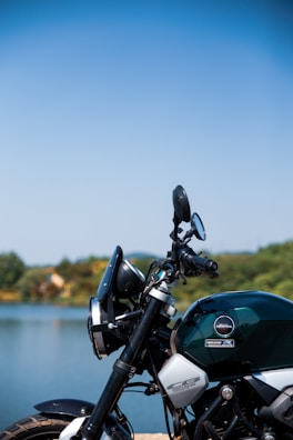 A motorcycle parked beside a tranquil lake surrounded by trees.