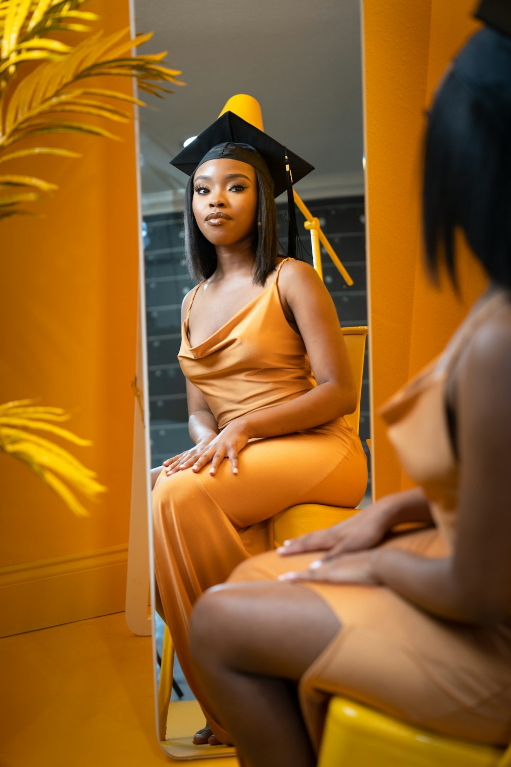 a woman sitting on a yellow chair wearing a graduation cap