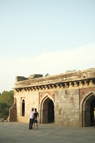 Two people embracing with the backdrop of a historic stone archway along the Camino route.