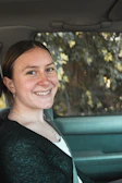 Close-up of a driver smiling inside a 4x4, surrounded by lush green forest.