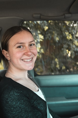 A smiling driver holding their driver's license next to their car with a GPS tracker visible.