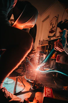 Workshop scene showing skilled hands welding a steel frame with sparks flying.