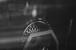 The black and white image features a close-up of a Goodyear tire. The tire appears to be on a display stand, with a reflective surface creating a somewhat abstract and moody ambiance. The tire's intricate tread pattern and the brand name are prominently visible.
