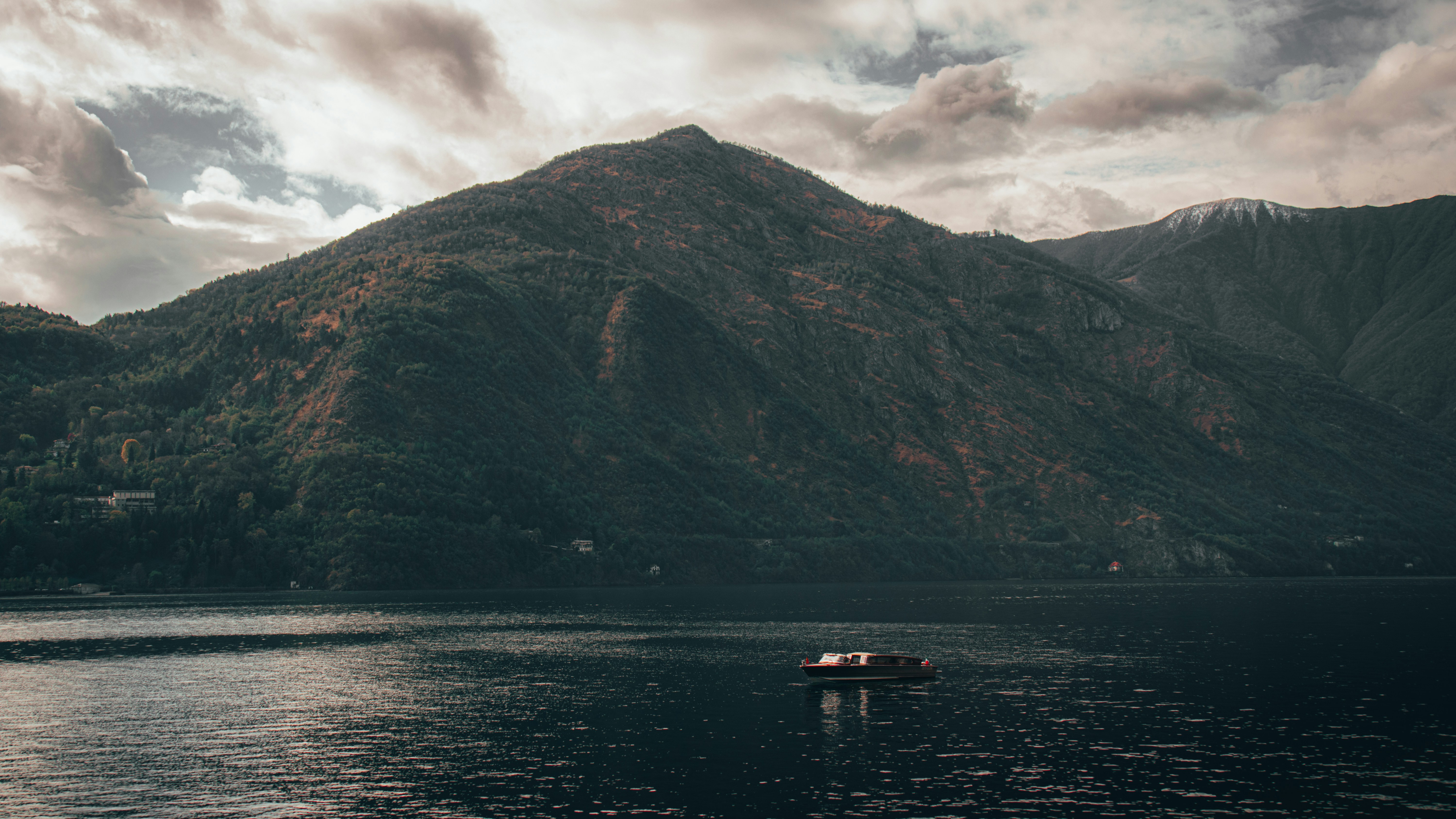 a boat floating on top of a lake next to a mountain, 