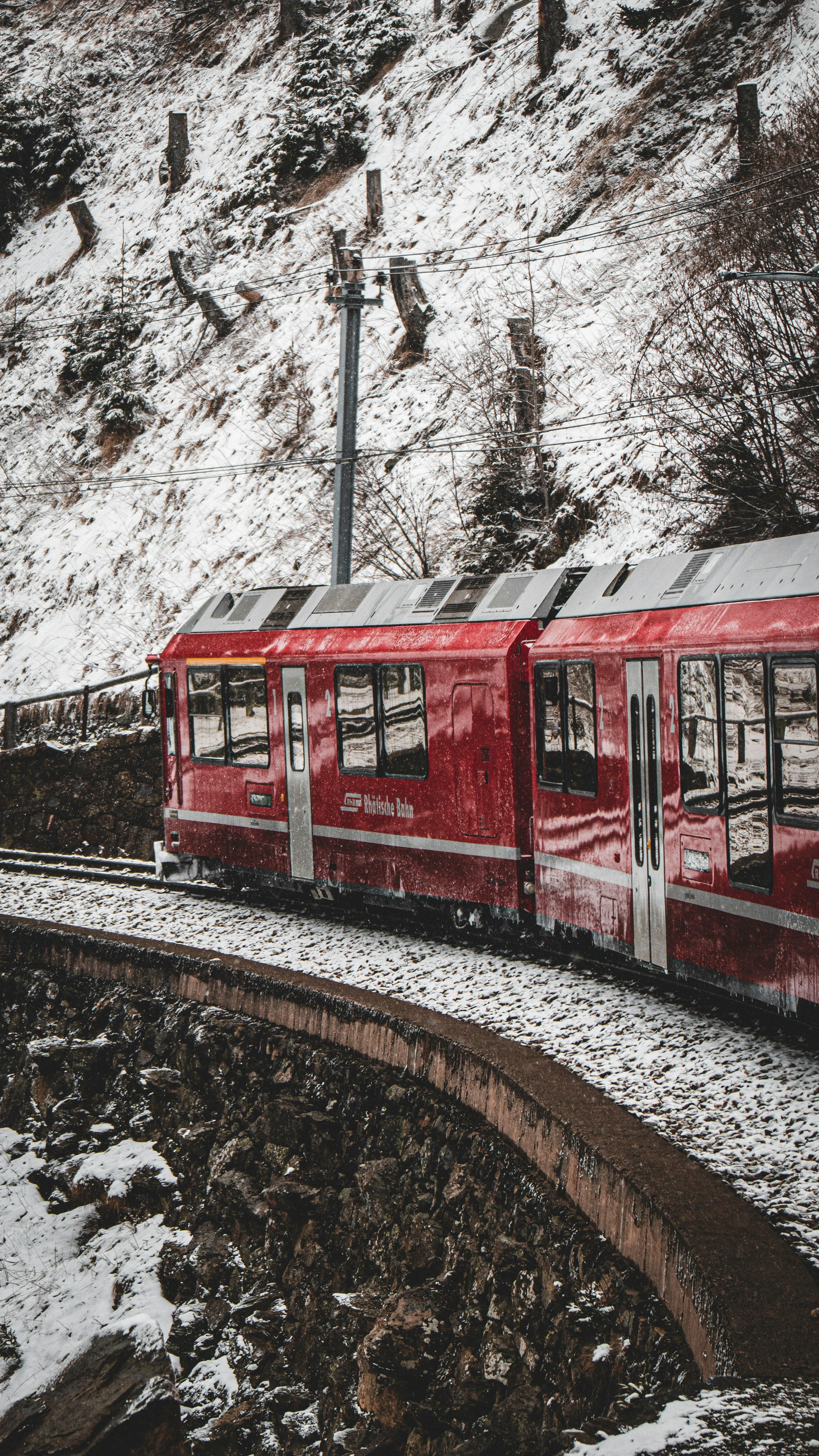 Ein roter Zug, der neben einem schneebedeckten Hang die Bahngleise hinunterfährt