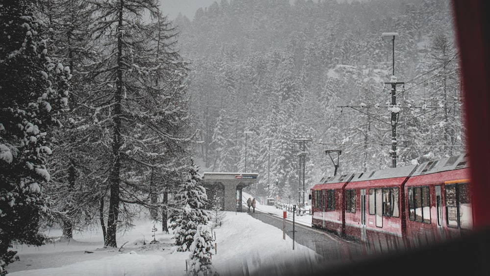 a red train traveling through a snow covered forest