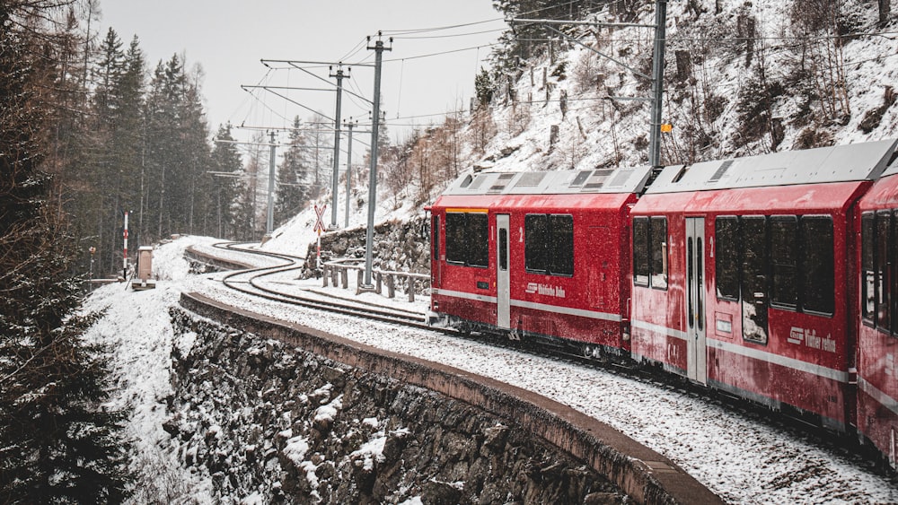 a red train traveling down train tracks next to a snow covered hillside