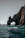 A glass-bottom boat navigates clear turquoise waters near a large natural rock arch formation. The sunlight casts shadows on the rugged surface of the rocks, and people in the boat are wearing life jackets.