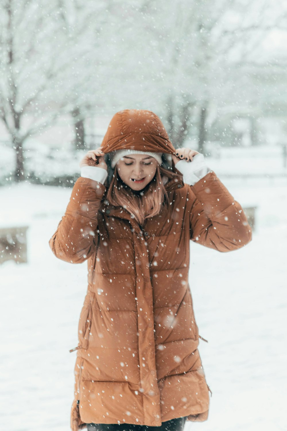 Una donna in piedi nella neve che indossa un cappotto marrone