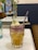 A vibrant cocktail sits elegantly on a marble table, featuring a blend of yellow and purple hues. The drink is garnished with a sprig of rosemary, a lime slice, and what appear to be lychee fruits. In the background, there are delicate pink flowers in vases, adding a touch of nature to the setting.