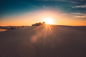 A serene Moroccan desert landscape at sunset with soft golden light and ancient ruins in the background.