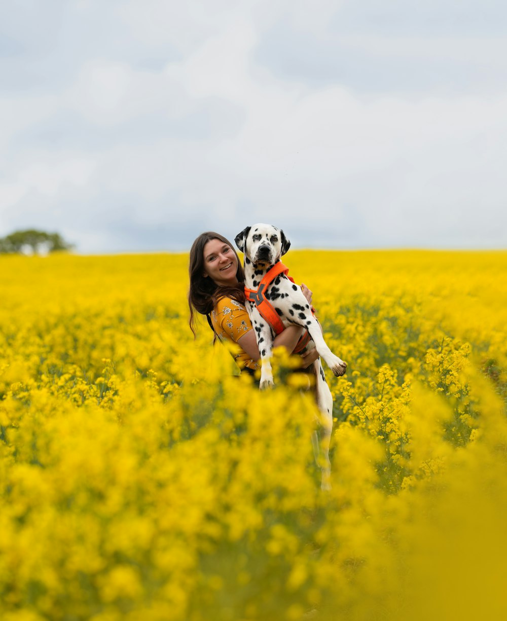 a woman holding a dalmatian dog in a field of yellow flowers