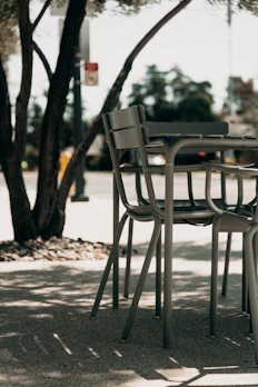 An elegant outdoor aluminum dining chair set against a sunlit patio backdrop.