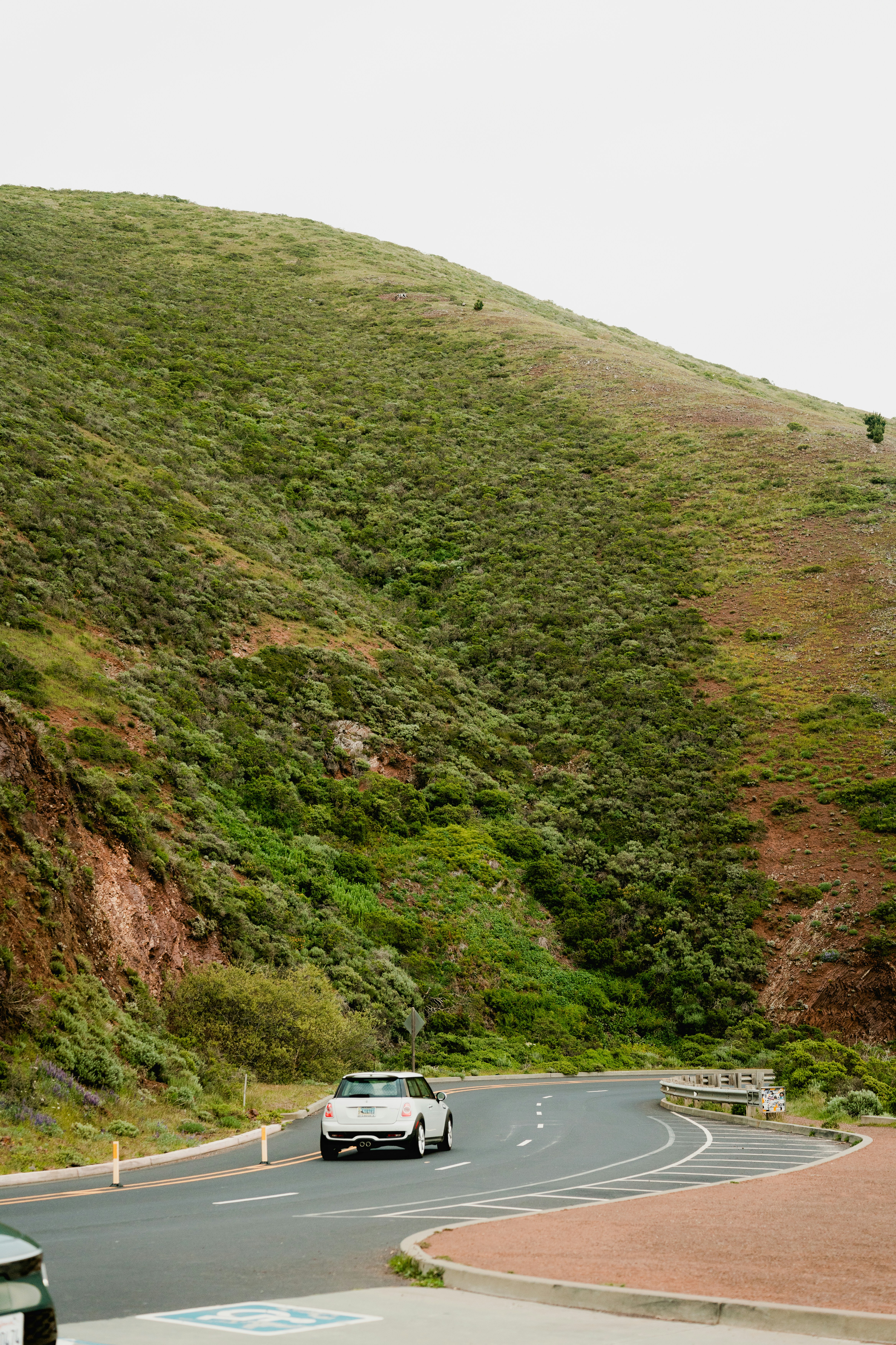 um carro dirigindo por uma estrada sinuosa ao lado de uma encosta verde exuberante