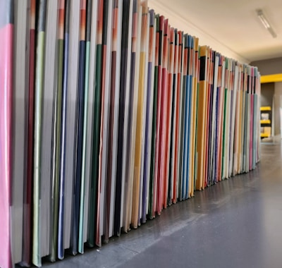 A neatly arranged row of colorful books or folders is lined up on a dark surface, with each cover adding a different hue to the sequence. The angle of the photo captures the long stretch of the arrangement, providing a sense of order and organization.