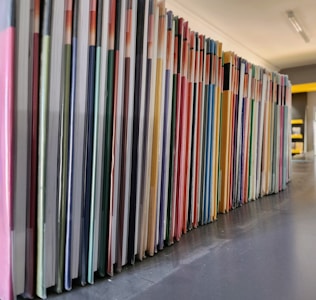 A neatly arranged row of colorful books or folders is lined up on a dark surface, with each cover adding a different hue to the sequence. The angle of the photo captures the long stretch of the arrangement, providing a sense of order and organization.