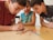 Three boys are deeply focused on what appears to be a game involving colorful wooden sticks, placed on a wooden table. They are leaning in closely, observing the sticks intently.