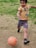 A young child dribbling a soccer ball on a grassy field, smiling with joy.