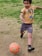 A young child dribbling a soccer ball on a grassy field, smiling with joy.