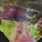 A vibrant mineral or crystal with a rough and uneven texture, showcasing a mixture of colors including green, blue, red, and yellow. The surface has a glassy appearance with natural fractures and imperfections, reflecting light in various directions.