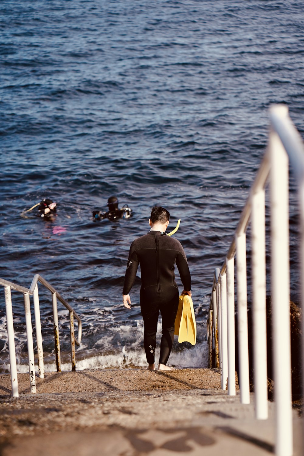 a man in a wet suit walking up a set of stairs towards the ocean