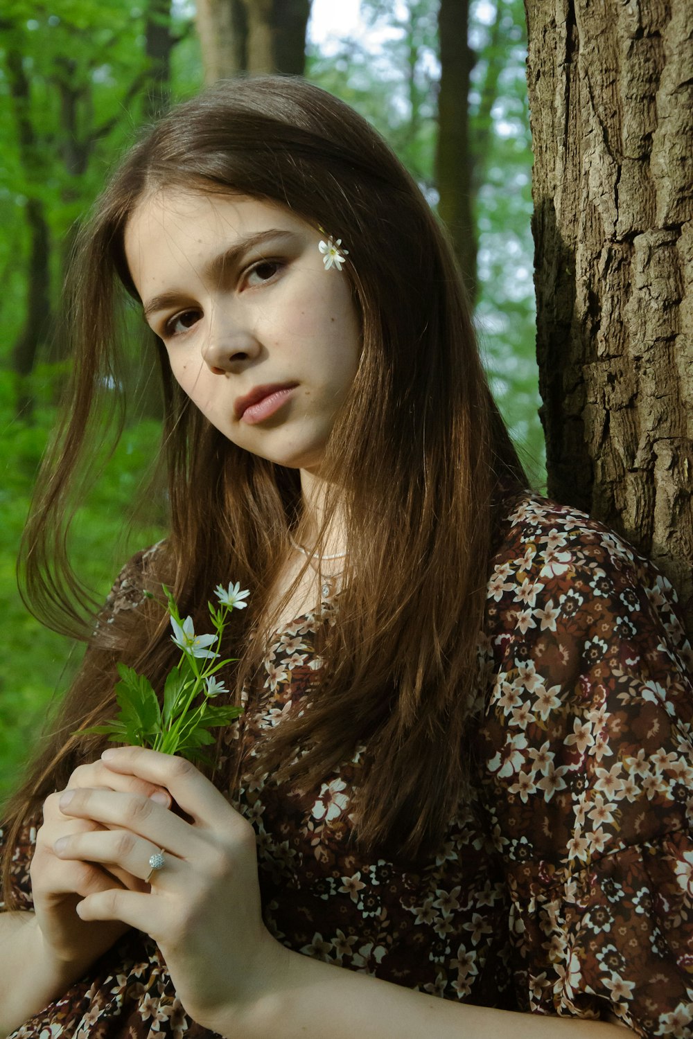 a girl in a dress holding a flower in front of a tree